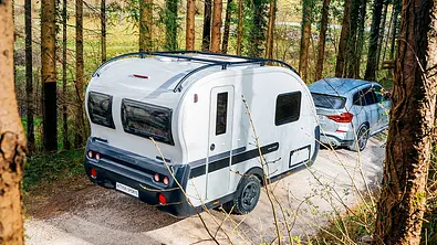 Der Adria Action Sports 391 LH (2025) von schräg hinten rechts von einem Auto gezogen auf einer Schotterstraße zwischen Bäumen. - Foto: Adria