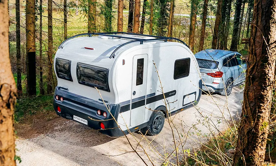 Adria Action Sports 391 LH (2025) Der Adria Action Sports 391 LH (2025) von schräg hinten rechts von einem Auto gezogen auf einer Schotterstraße zwischen Bäumen.