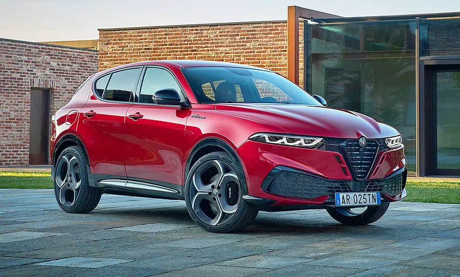 Alfa Romeo Tonale Facelift (2025) Das Alfa Romeo Tonale Facelift (2025) steht vor einem modernen Haus, von vorne rechts fotografiert.