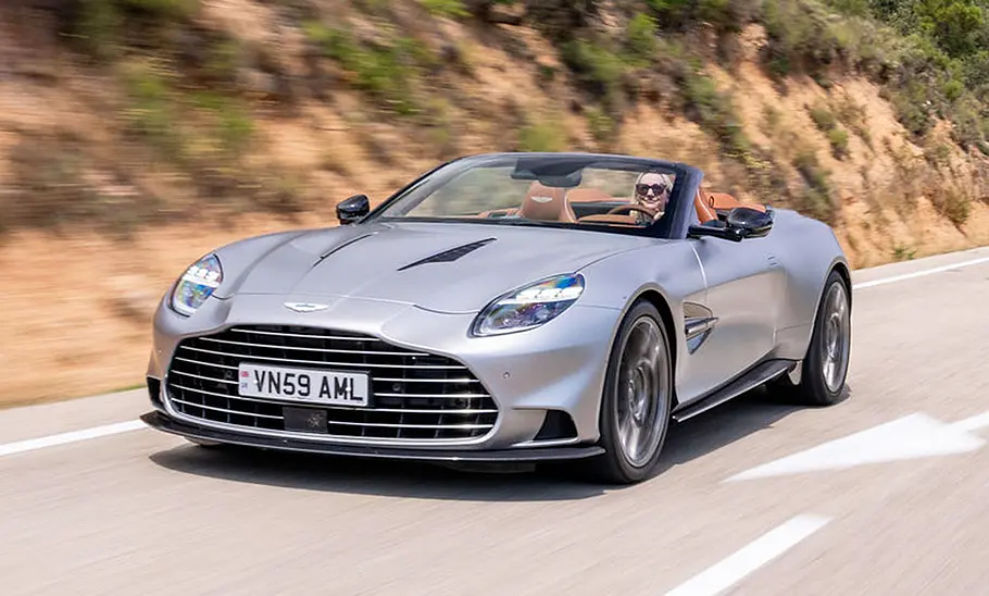 Aston Martin Vanquish Volante (2025) Der Aston Martin Vanquish Volante (2025) fährt mit offenem Dach über eine Landstraße, von vorne links fotografiert.