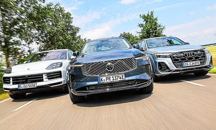 Blick von vorne auf die drei SUV Porsche Cayenne, Volvo XC90 und Audi Q7, die in Formation nebeneinander herfahren.