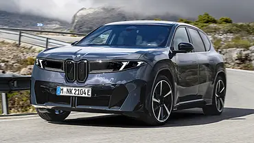 Der BMW iX3 fährt auf einer Bergstraße durch eine Rechtskurve, von vorne links fotografiert. - Foto: BMW