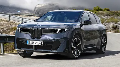 Der BMW iX3 fährt auf einer Bergstraße durch eine Rechtskurve, von vorne links fotografiert. - Foto: BMW
