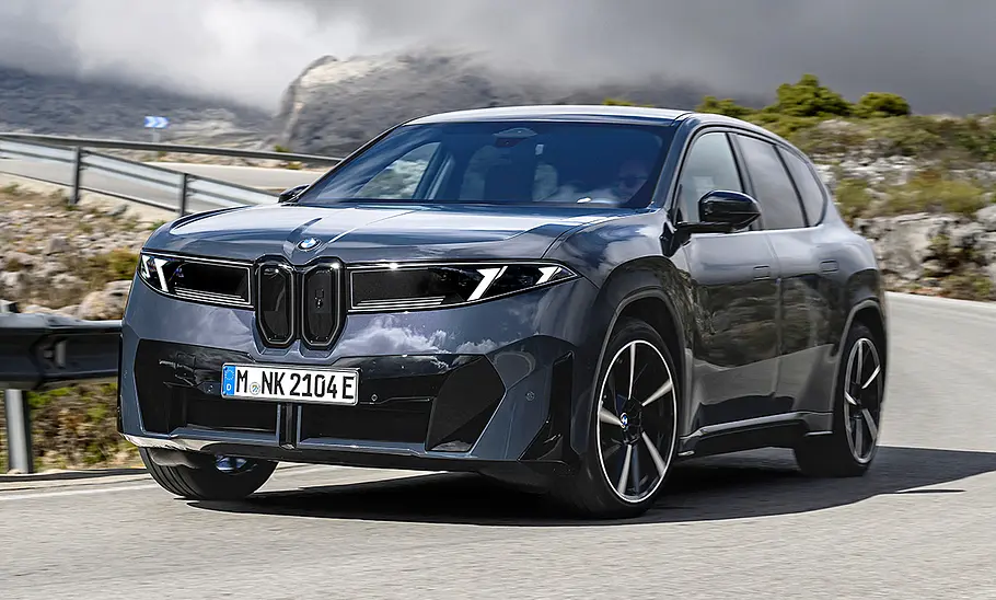 BMW iX3 Der BMW iX3 fährt auf einer Bergstraße durch eine Rechtskurve, von vorne links fotografiert.