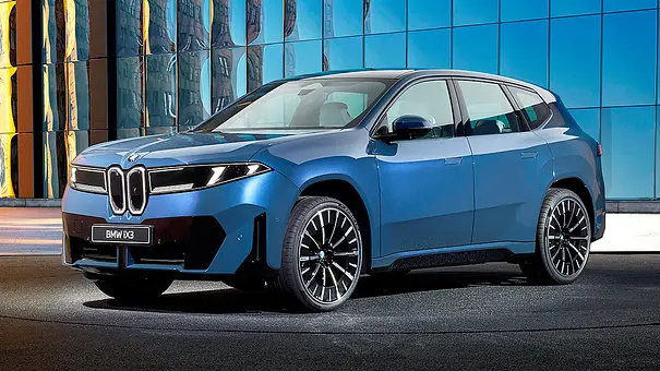 Der BMW iX3 (2026) steht vor einer Glasfassade, von vorne links fotografiert. - Foto: BMW