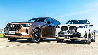 Blick von schräg vorne auf die beiden fahrenden SUV Mazda CX-80 und BMW X3. - Foto: Frank Ratering