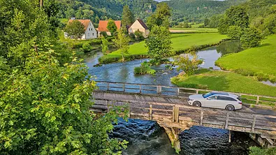 Das Mercedes E 220 d 4Matic T-Modell fährt über eine Holzbrücke. Im Hintergrund eine idyllische Landschaft und Häuser. - Foto: Hardy Mutschler