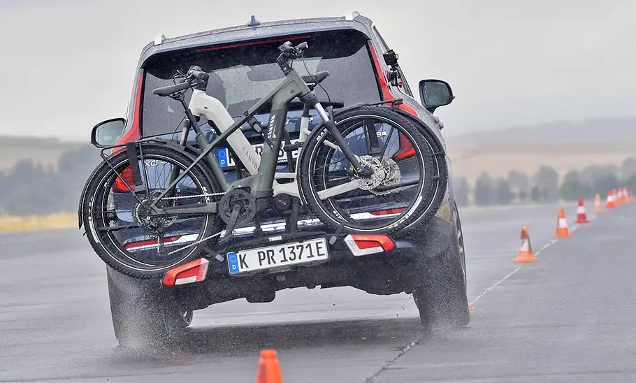 Thule-Fahrradträger für bis zu drei E-Bikes im Test Der mit zwei E-Bikes beladene Thule-Heckträger Easyfold 3 auf dem Testwagen montiert bei der Slalomfahrt auf einer regennassen Teststrecke.