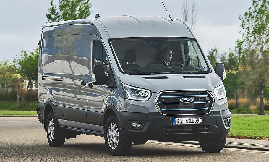 Der Ford E-Transit (2022) fährt durch eine Linkskurve, von vorne rechts fotografiert.