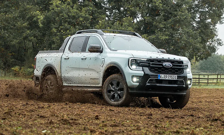 Der Ford Ranger Plug-in-Hybrid (2025) driftet auf einer Weide durch eine Rechtskurve und schleudert Erde auf, von vorne rechts fotografiert.