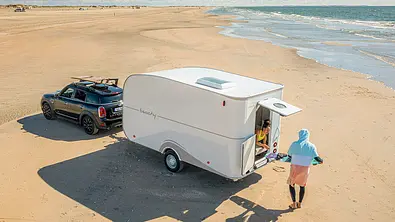 Die Außenaufnahme zeigt den Hobby Beachy 420+ (2025) statisch von schräg hinten links an einem Strand stehend. - Foto: Hobby