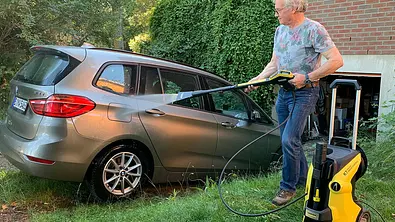 Das Bild zeigt den Kärcher eco!Booster-Düse im Test. Eine Person wäscht mit einem Hochdruckreiniger einen in einer Garageneinfahrt geparkten BMW 2er Gran Tourer. - Foto: Holger Ippen