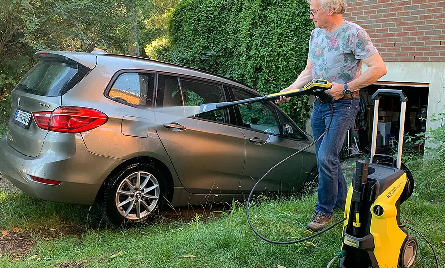 Das Bild zeigt den Kärcher eco!Booster-Düse im Test. Eine Person wäscht mit einem Hochdruckreiniger einen in einer Garageneinfahrt geparkten BMW 2er Gran Tourer.