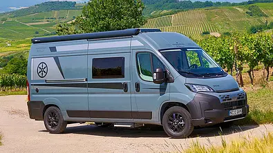 Das Bild zeigt den Karmann Davis 590 TS (2025) statisch von schräg vorne rechts fotografiert. Im Hintergrund sind Weinberge zu sehen. - Foto: Karmann Mobil