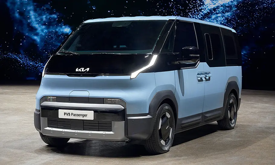 Kia PV5 Passenger (2025) Der Kia PV5 Passenger (2025) steht in Studioumgebung, von vorne links fotografiert.
