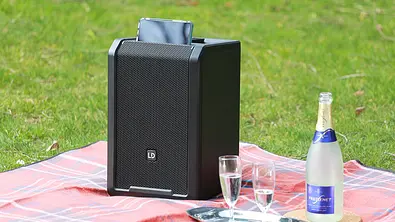 LD Systems Anny 8 Soundsystem auf einer Campingdecke mit Sekt und zwei Gläsern, fotografiert von vorn. - Foto: Holger Ippen
