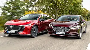 Mazda6e und Mazda6 fahren nebeneinander auf einer Landstraße, von vorne links fotografiert. - Foto: Frank Ratering