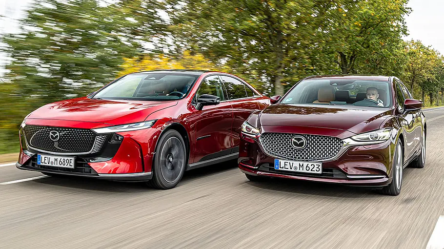 Mazda6e und Mazda6 fahren nebeneinander auf einer Landstraße, von vorne links fotografiert.