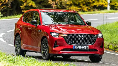 Der Mazda CX-60 fährt auf einer Landstraße eine Linkskurve. Ansicht des Fahrzeugs von vorne rechts. - Foto: Frank Ratering