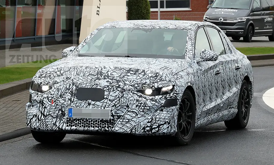Die Mercedes E-Klasse EQ (2027) fährt als Erlkönig aus einem Kreisverkehr, von vorne fotografiert.