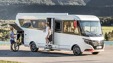 Niesmann + Bischoff iSmove (2024) parkt auf einer asphaltierten Fläche, eine Person lädt ein Fahrrad in die Heckgarage, eine andere Person steht in der Eingangstür. - Foto: Niesmann + Bischoff Niesmann + Bischoff iSmove (2024) parkt auf einer asphaltierten Fläche, eine Person lädt ein Fahrrad in die Heckgarage, eine andere Person steht in der Eingangstür. - Foto: Niesmann + Bischoff