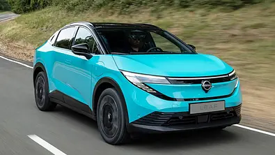 Der Nissan Leaf (2025) fährt auf einer Landstraße, von vorne rechts fotografiert. - Foto: Nissan