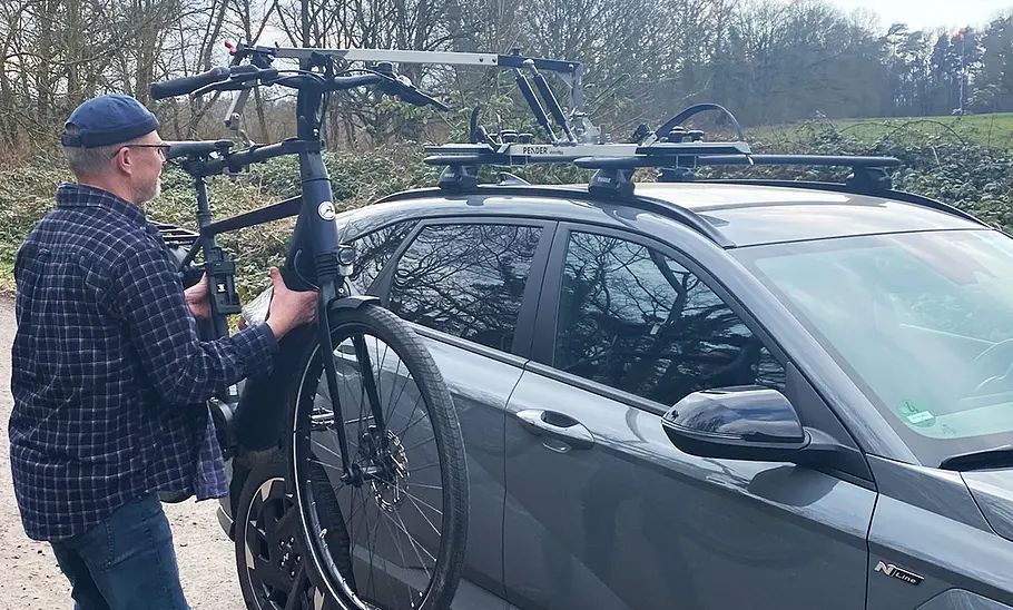 Test-Redakteur beim Heben eines E-Bikes aufs Autodach mit dem Pender Ebikelifter.