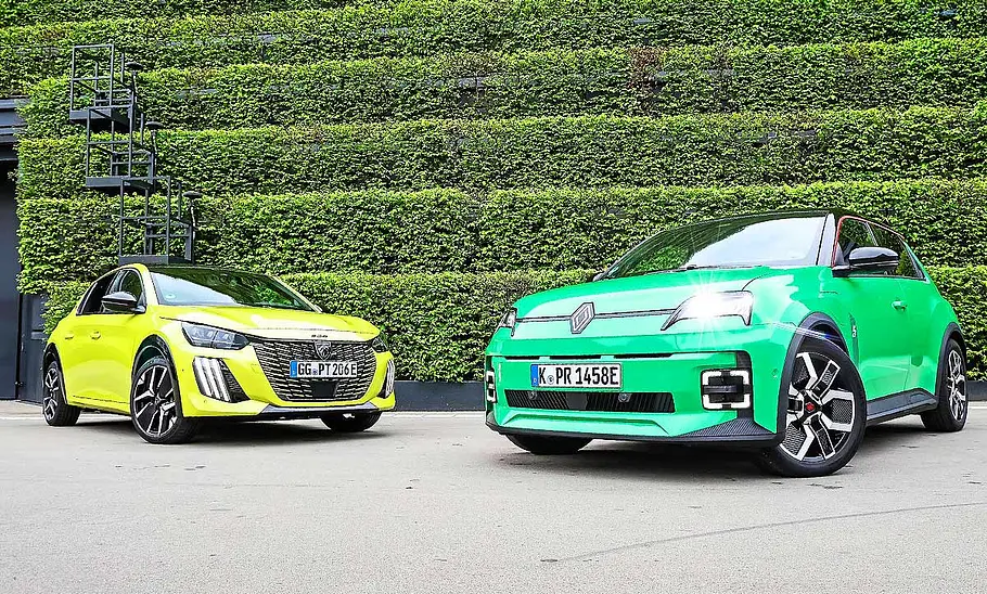 Gruppenbild mit den zwei elektrischen Kleinwagen Peugeot E-208 und Renault 5; Blick von schräg vorne auf die Autos.