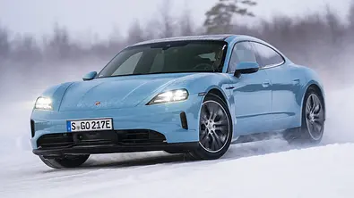 Das Porsche Taycan 4 Facelift (2025) driftet im Schnee durch eine Linkskurve, von vorne links fotografiert. - Foto: Porsche