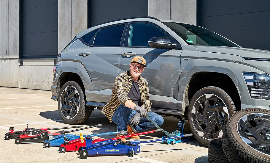 Tester mit sechs Rangierwagenhebern, Auto und Reifenstapel, fotografiert von der Seite.