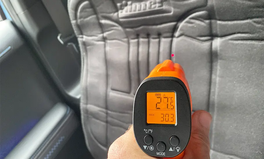 Das Foto zeigt ein Infrarotthermometer im Versuchsaufbau mit der auf dem Autositz montierten Heizauflage.