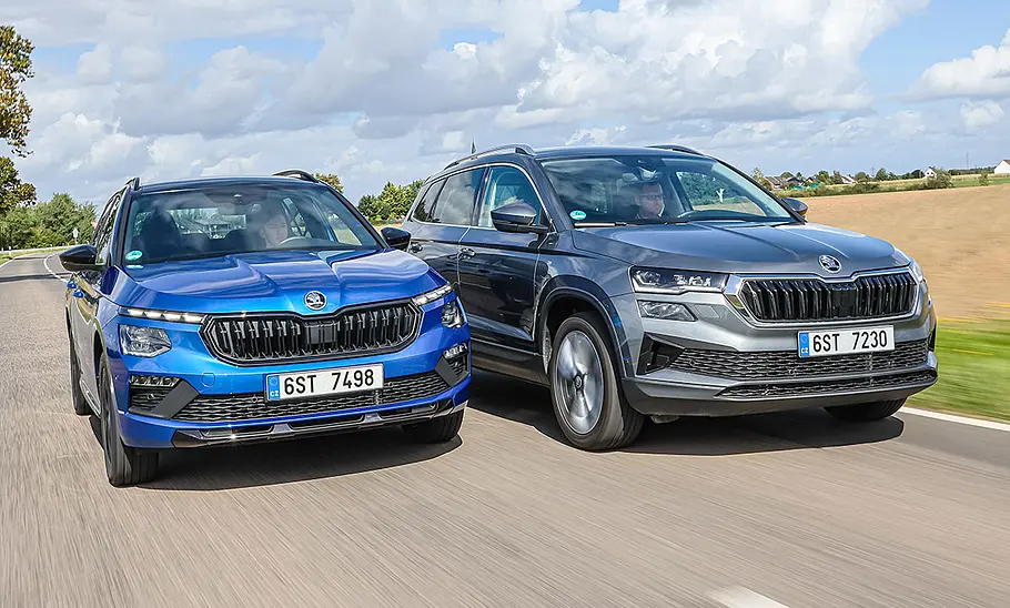 Skoda Kamiq und Skoda Karoq fahren nebeneinander auf einer Landstraße, von vorne fotografiert.