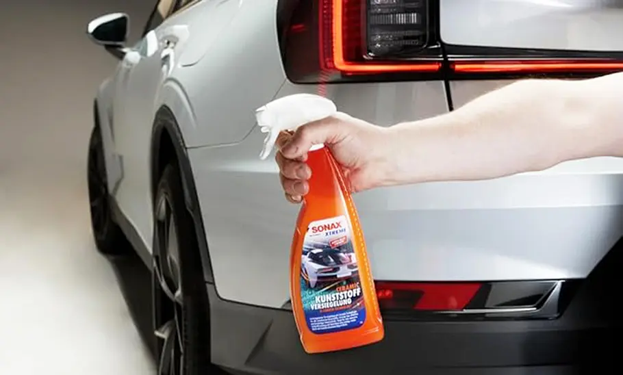 Heckansicht eines Autos mit Hand und Sonax Kunststoffversiegelung.