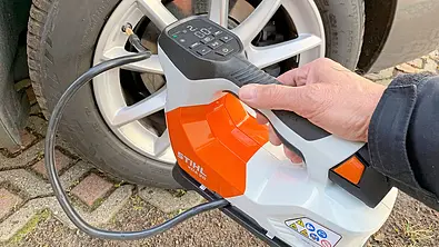 Stihl Akku-Kompressor KOA 20 im Test am Autoreifen mit Hand am Gerät. - Foto: Holger Ippen