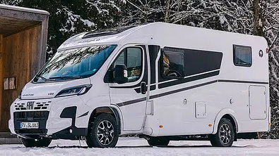 Der Sunlight V66 statisch von schräg vorne links. Das Wohnmobil steht im Schnee vor einem Unterstand, im Hintergrund ist ein verschneiter Nadelbaumwald zu sehen. - Foto: Sunlight