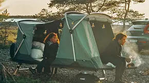 Thule Outset (2024) auf Stelzen aufgebaut, zwei Personen sitzen in den geöffneten Zelteingängen. - Foto: Thule Thule Outset (2024) auf Stelzen aufgebaut, zwei Personen sitzen in den geöffneten Zelteingängen. - Foto: Thule