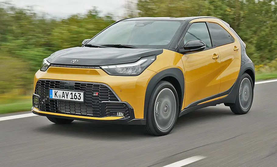 Toyota Aygo X Facelift (2025) fährt auf einer Landstraße, Ansicht von vorne links.