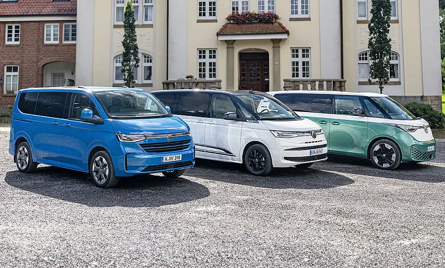 VW Caravelle/Multivan/ID. Buzz VW Caravelle, Multivan und ID. Buzz stehen nebeneinander auf einem Schotterparkplatz.