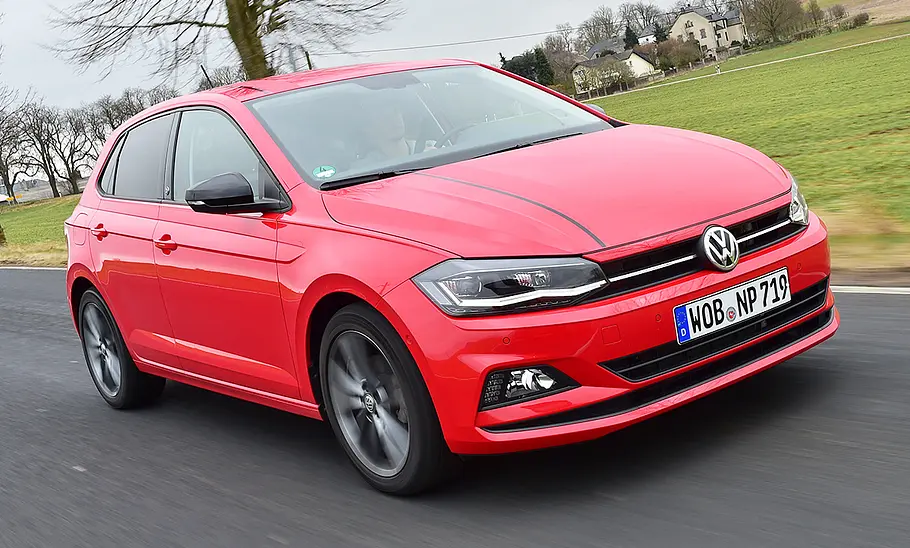 Der VW Polo (2017) fährt über eine Straße, im Hintergrund ist eine Wiese zu sehen. Von vorne rechts fotografiert.