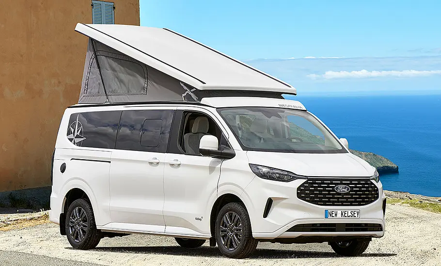 Die Außenaufnahme zeigt einen Westfalia Kelsey (2025) mit aufgeklapptem Dach auf einem Hügel am Meer, Ansicht von vorne rechts.