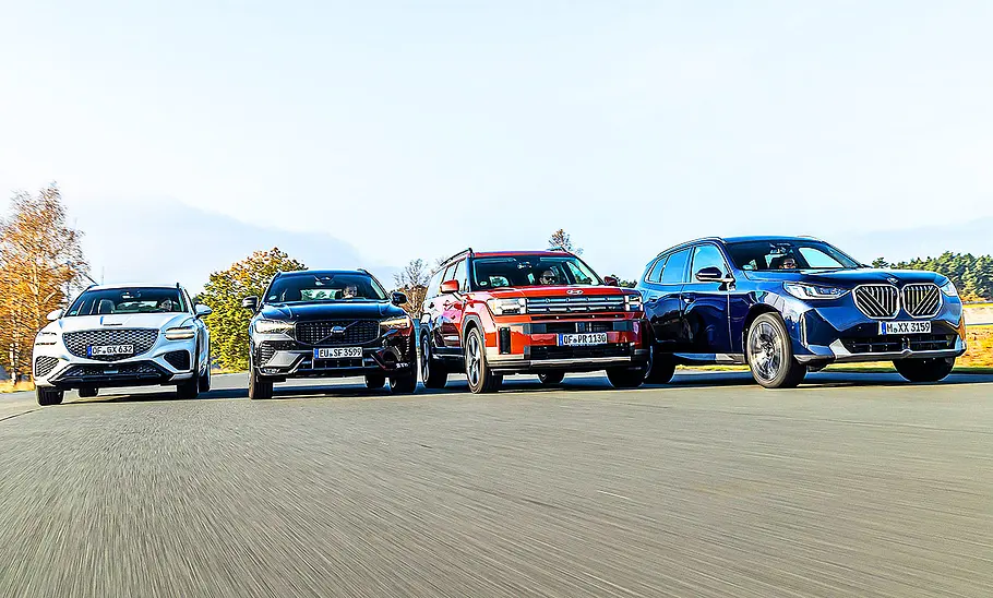 Genesis GV70/Volvo XC60/Hyundai Santa Fe/BMW X3 Gruppenbild mit frontaler Ansicht auf Genesis GV70, Volvo XC60, Hyundai Santa Fe & BMW X3, die nebeneinander herfahren.