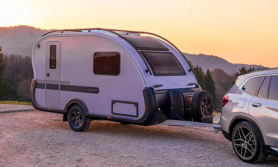 Adria Action Sports 391 LH (2025) Der Adria Action Sports 391 LH (2025) statisch im Sonnenuntergang von schräg vorne rechts an einem Auto angehängt. Im Hintergrund sind Hügel zu sehen.