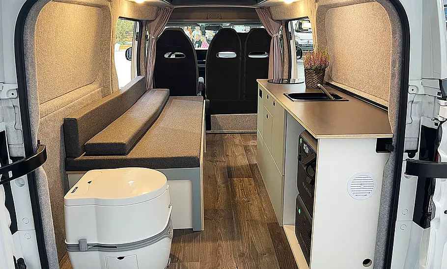 Die Innenaufnahme zeigt den Wohnraum des Alpincamper Maxus eDeliver 5 (2025) mit Blick durch die Hecktüren nach vorne.