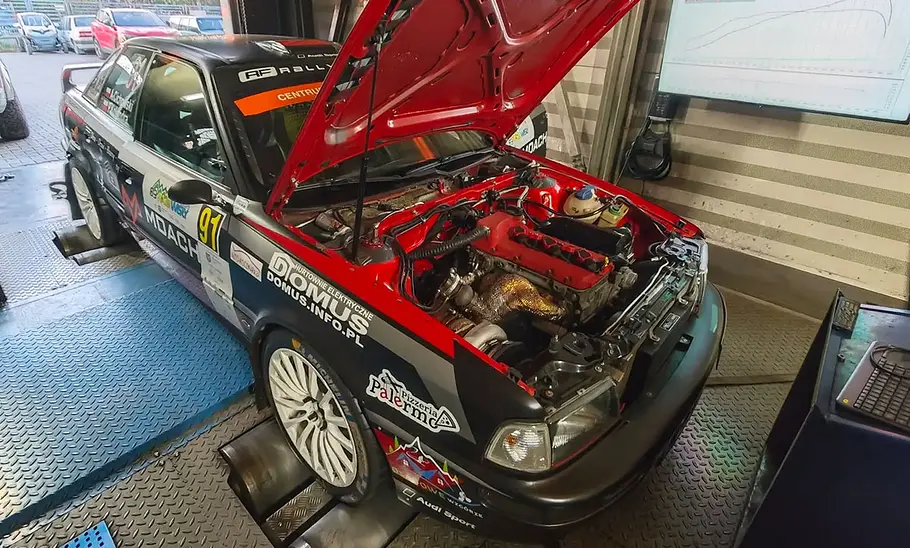 Der Audi 80 VR5T mit offener Motorhaube bei Leistungsprüfung auf dem Prüfstand, fotografiert von schräg vorne.