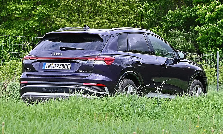 Audi Q4 45 e-tron Audi Q4 45 e-tron auf einer Landstraße von hinten, teils von Wiese verdeckt.
