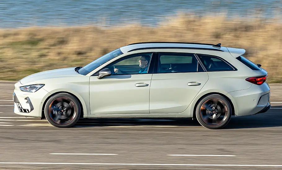 Cupra Leon Sportstourer Der Cupra Leon Sportstourer fährt auf einer Straße an einer Düne entlang, von links fotografiert.