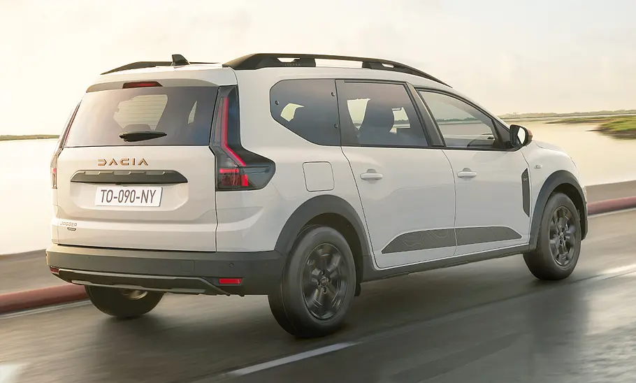 Das Dacia Jogger Facelift (2026) fährt auf einer Straße am Wasser, von hinten rechts fotografiert.