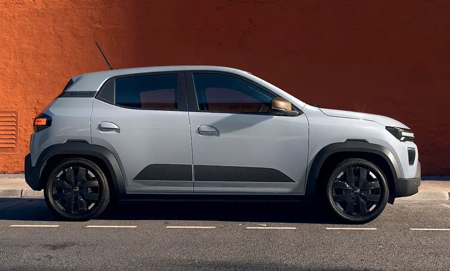 Dacia Spring Facelift (2024) Das Dacia Spring Facelift (2024) parkt vor einer Fassade, von rechts fotografiert.