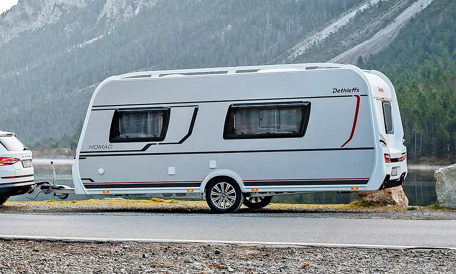 Dethleffs Nomad 490 EST (2025) Dethleffs Nomad 490 EST (2025) hängt an einem Auto, Ansicht von der linken Seite. Im Hintergrund ein Tal in den Bergen.