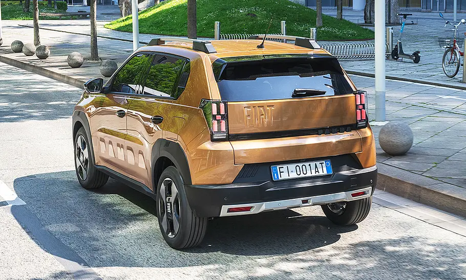 Der Fiat Grande Panda Hybrid (2025) fährt durch eine Stadt, von hinten links fotografiert.
